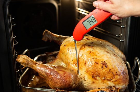 A red Thermapen, digital food thermometer being used to measure the temperature of a turkey coming out the oven