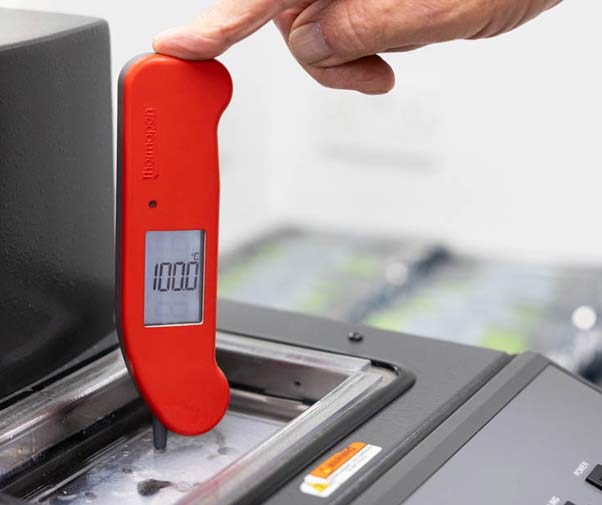 Finger and hand visible to hold the Thermapen ONE in red in place for an accuracy check in a calibration bath, screen is reading 100 degrees