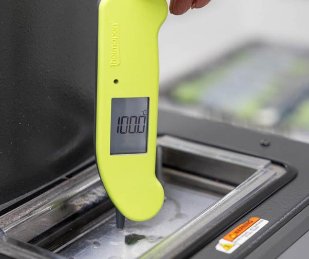 Finger and hand visible to hold the Thermapen ONE in Hi-Vis in place for an accuracy check in a calibration bath, screen is reading 100 degrees